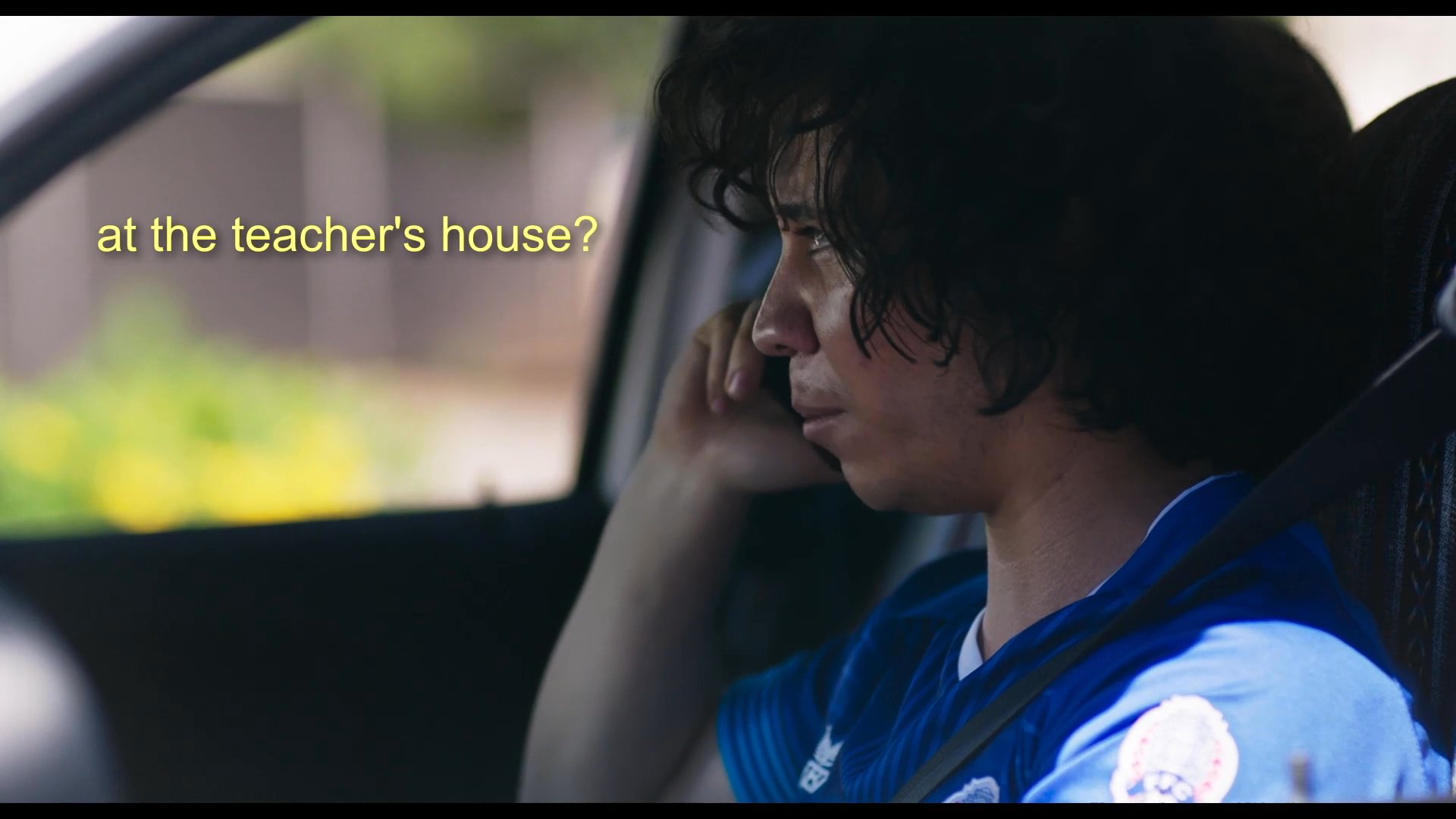 A young man calls his mother to ask a question about driver's education while she carries out chores around the house. The scene juxtaposes the mundane domestic activity with the specific inquiry about educational logistics.