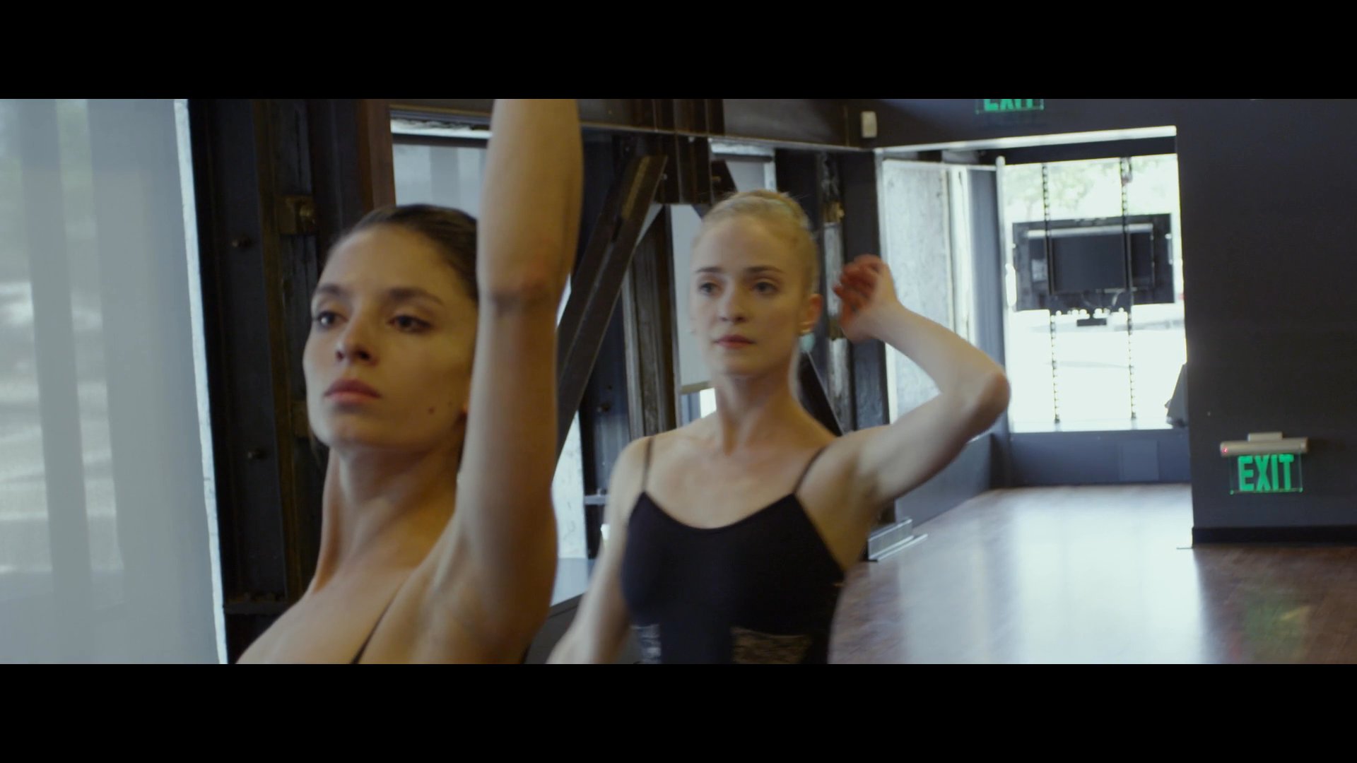 Professional dancers practice complex choreography in a mirror-walled studio under the guidance of an instructor. The session focuses on refining technical movements and coordination for an upcoming performance.