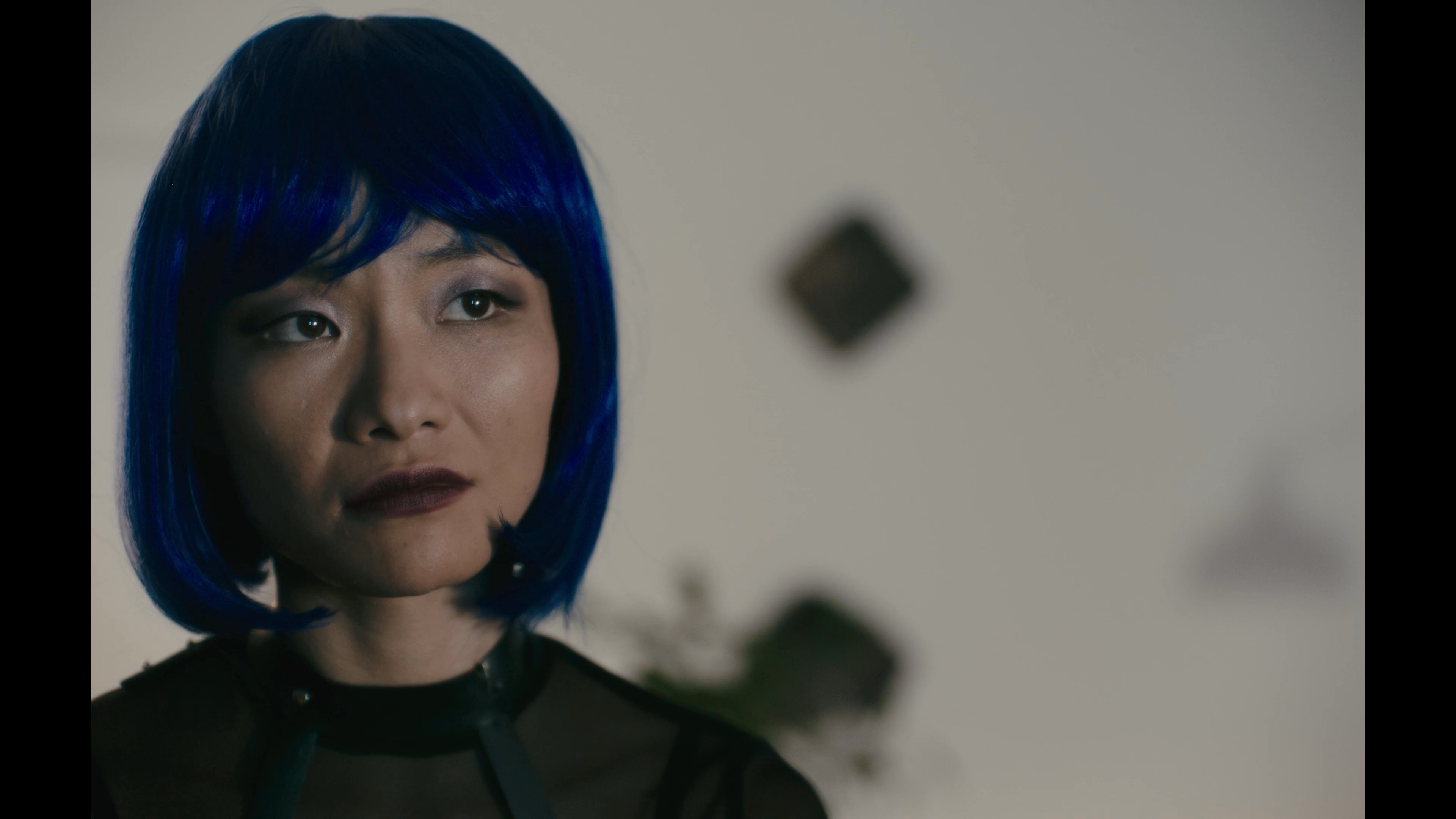 A man in a business suit experiments with a VR headset while engaging in a serious conversation with a woman wearing a blue wig. The scene transitions between his technological setup and their focused, tense interaction.