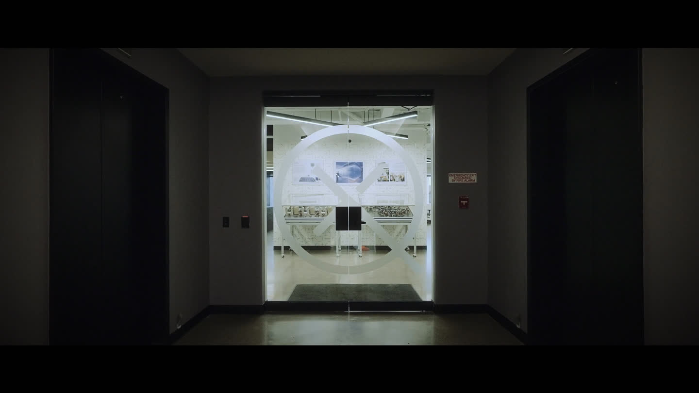 Film still: the Xanadu symbol on glass doors leading into the workplace