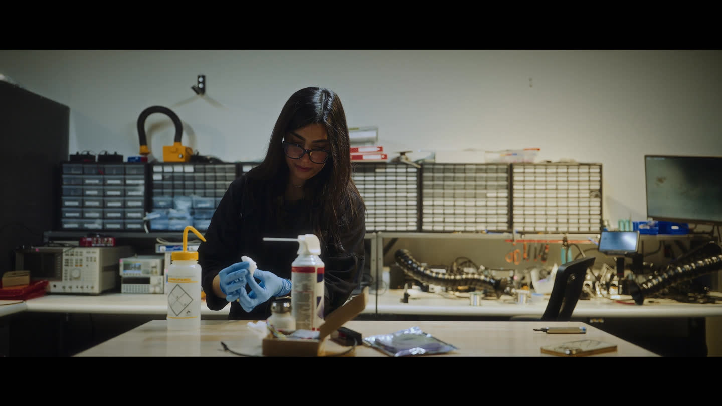 Film still: a Xanadu team member wearing gloves at a laboratory workbench