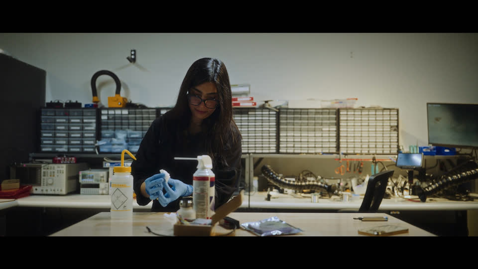 Film still: a Xanadu team member wearing gloves at a laboratory workbench