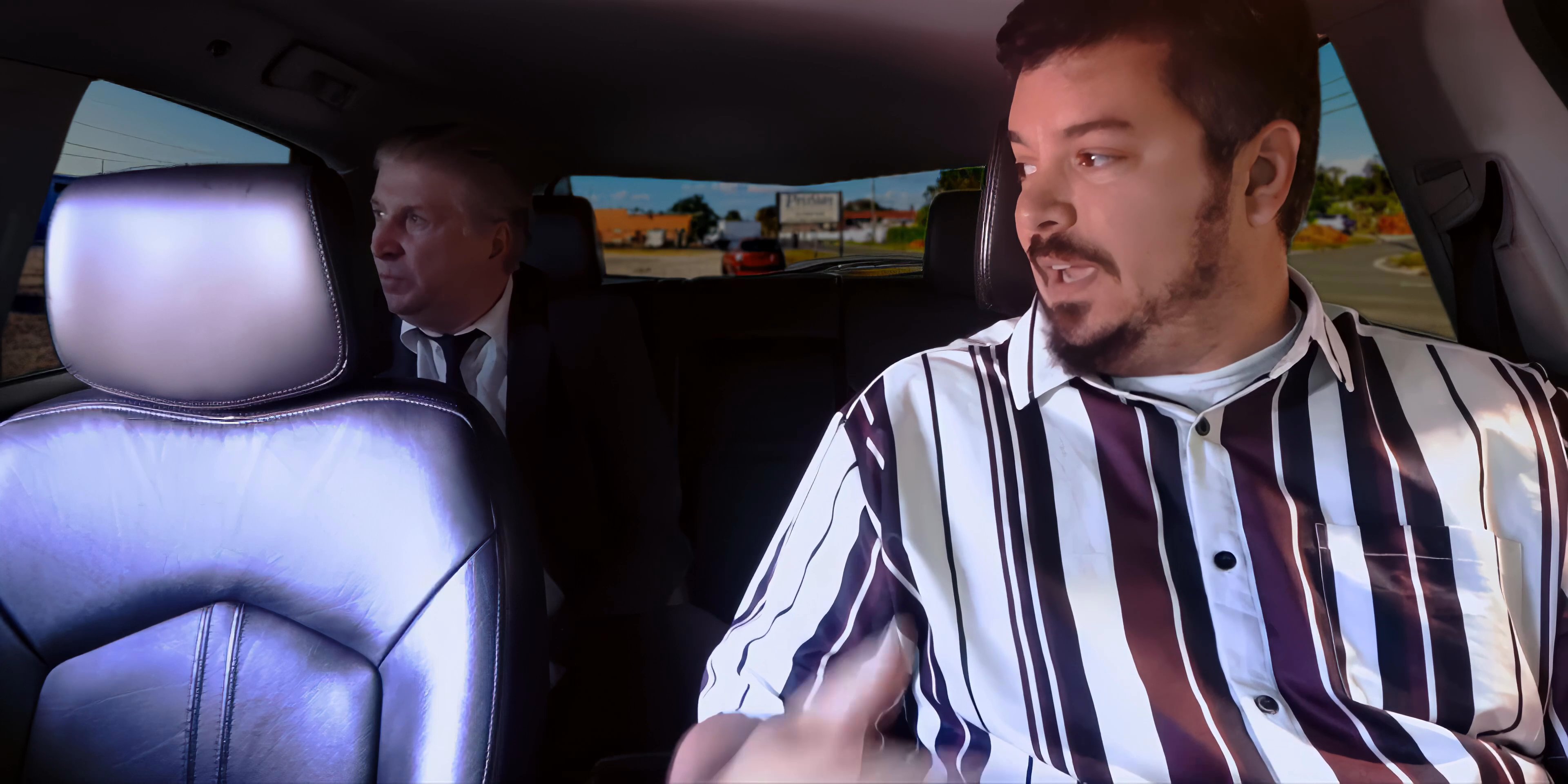 Two men engage in a serious discussion while seated inside the rear of a moving vehicle. The interaction focuses on dialogue exchanged between the individuals during their transit.