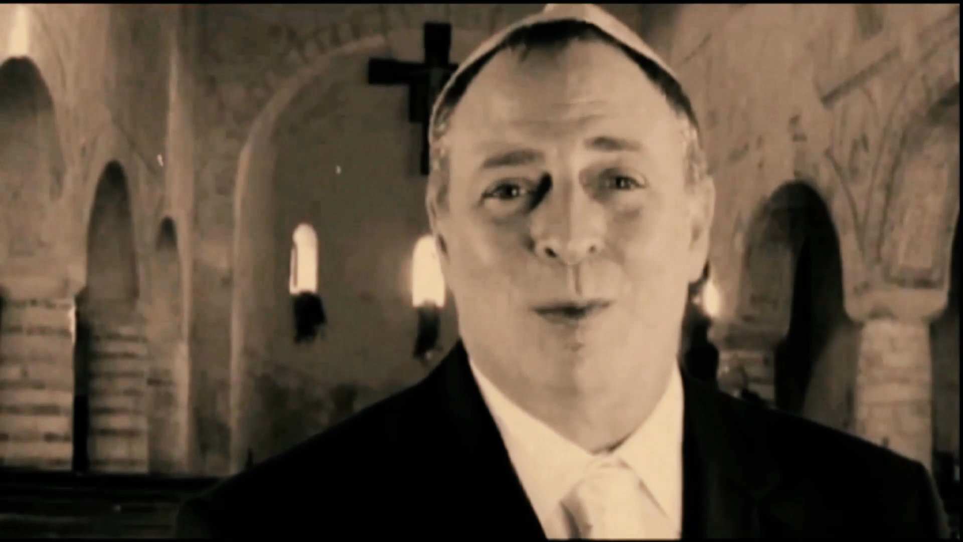 A man in clerical attire delivers a heartfelt oration from within a dimly lit stone cathedral.