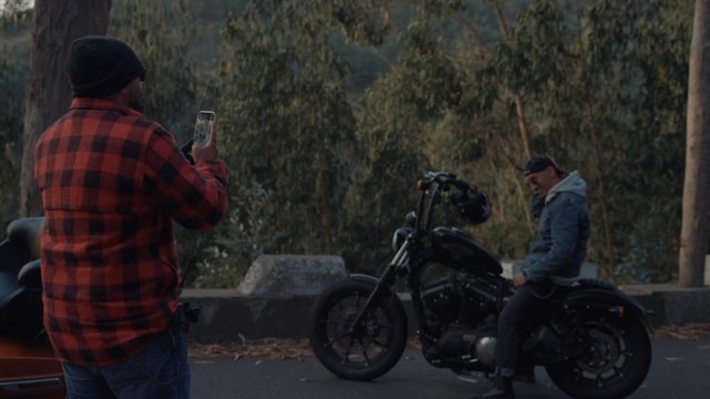 A man taking photos of his friend posing on a motorcycle