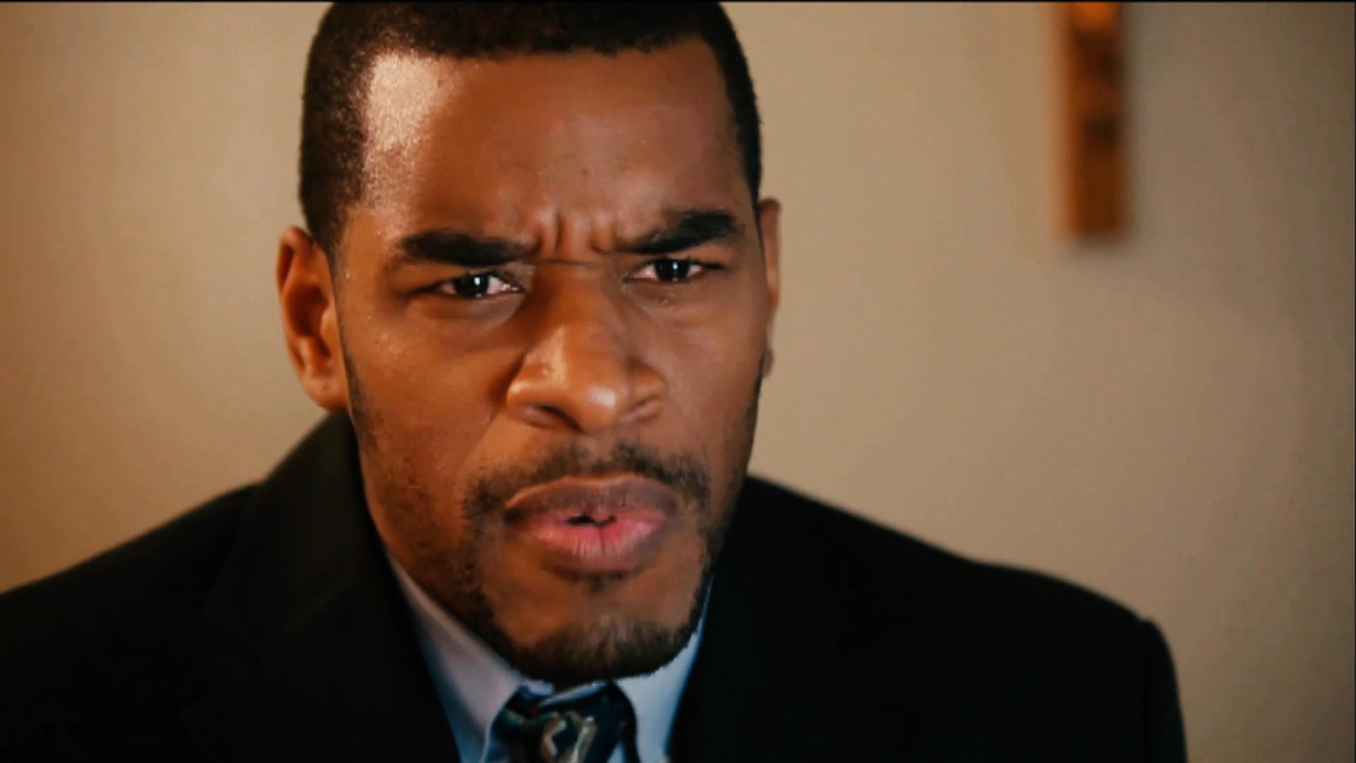 A man in a suit delivers an impassioned sermon to a church congregation while gesturing toward a Bible. His expressive delivery emphasizes spiritual instruction in a formal sanctuary setting.