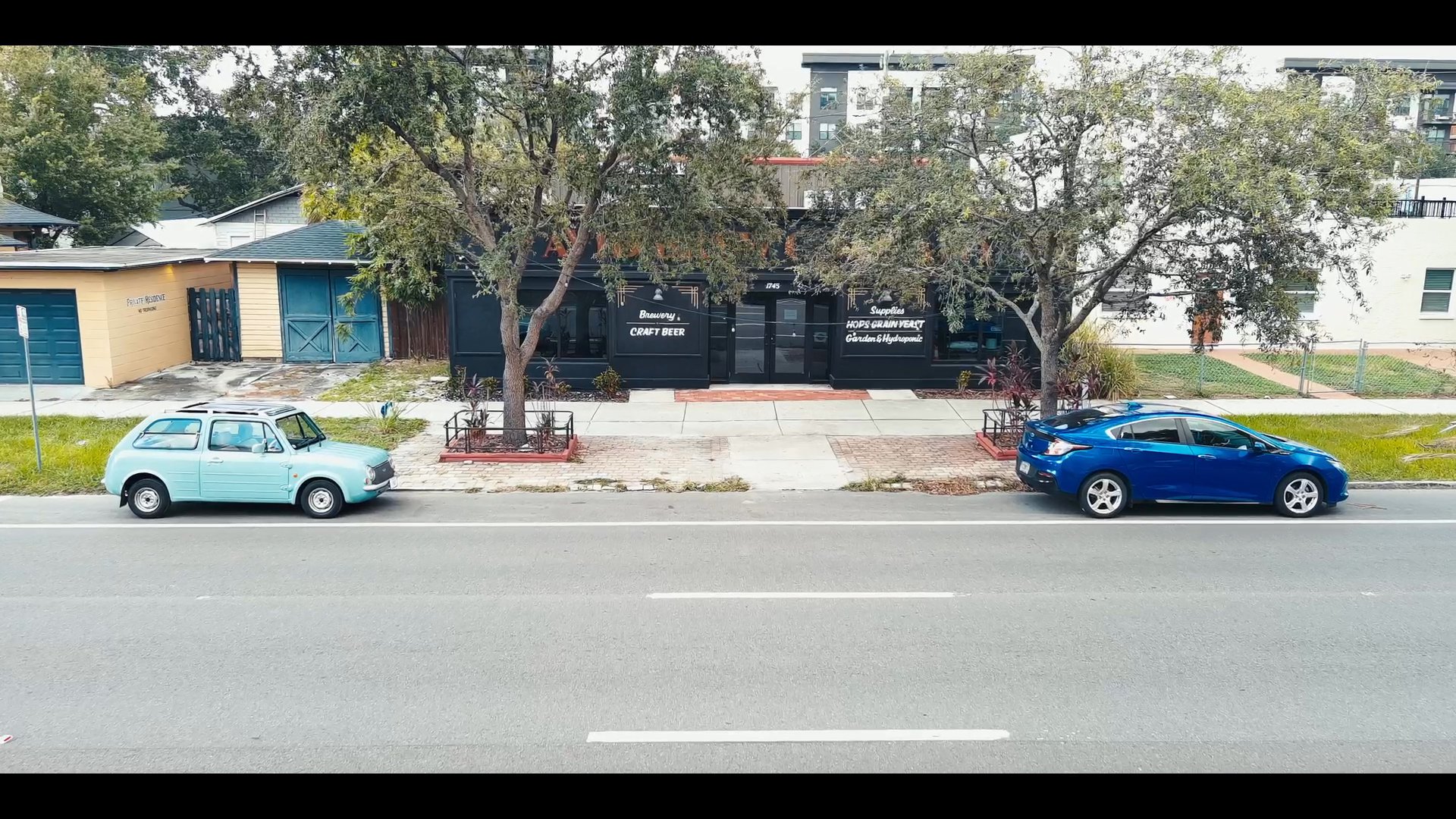 A man monitors a city environment before transitioning to a brewery setting where a delivery box is presented and discussed between two individuals.