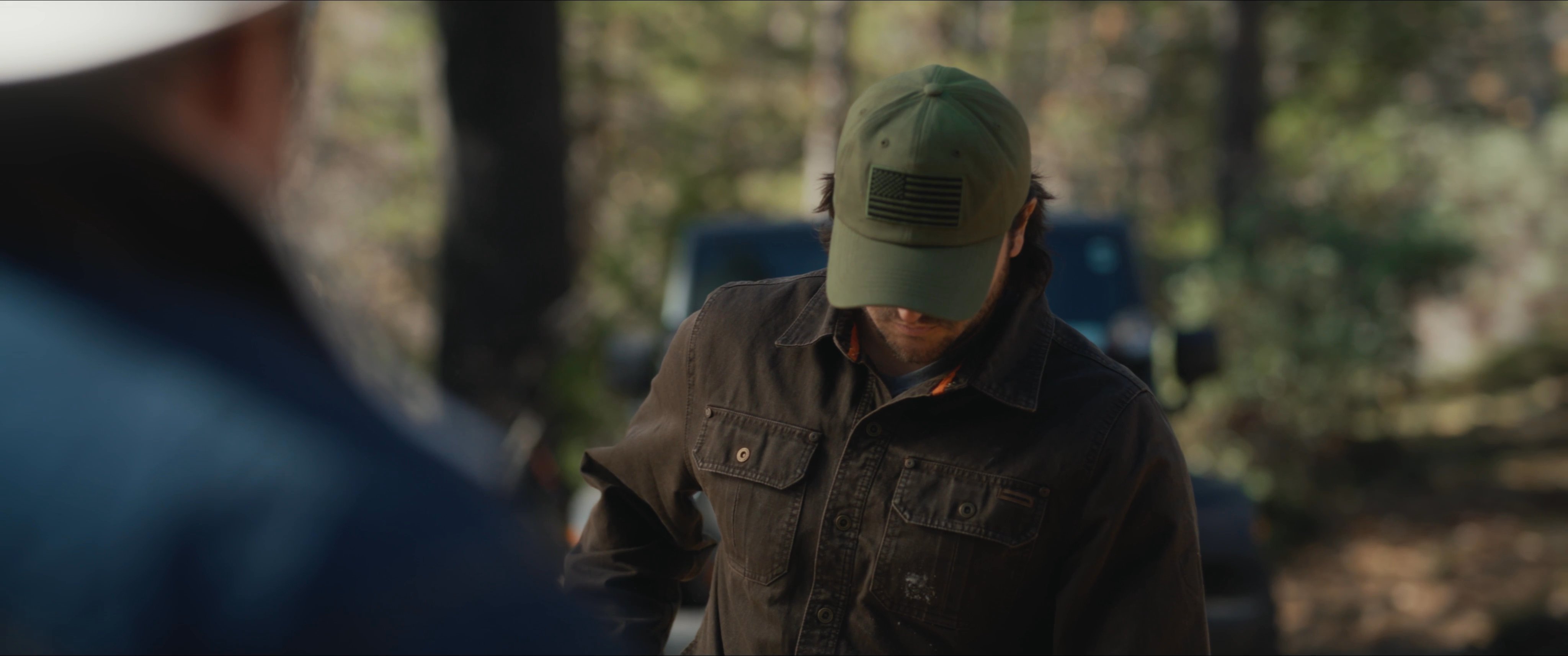 Two men engage in a tense conversation within a wooded area, alternating between close-up character shots to capture the weight of their interaction.