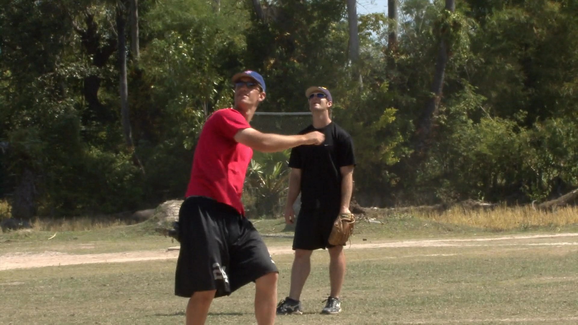 Athletes perform physical conditioning and fitness drills under the supervision of a coach in an outdoor setting before transitioning to baseball practice on a field.
