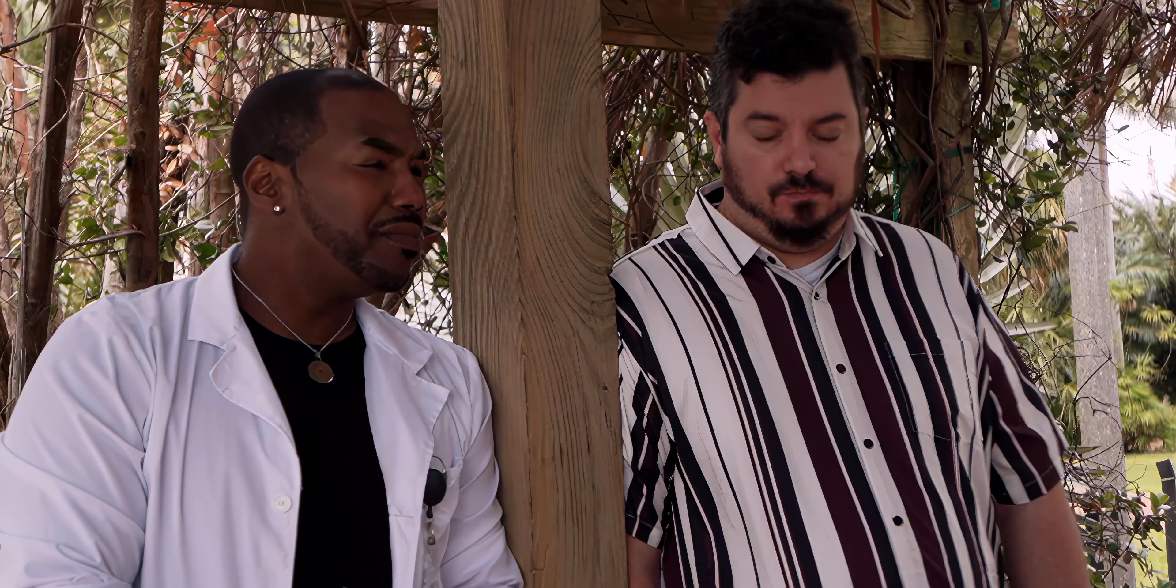 Two men engage in a calm, focused conversation while standing in an outdoor setting.