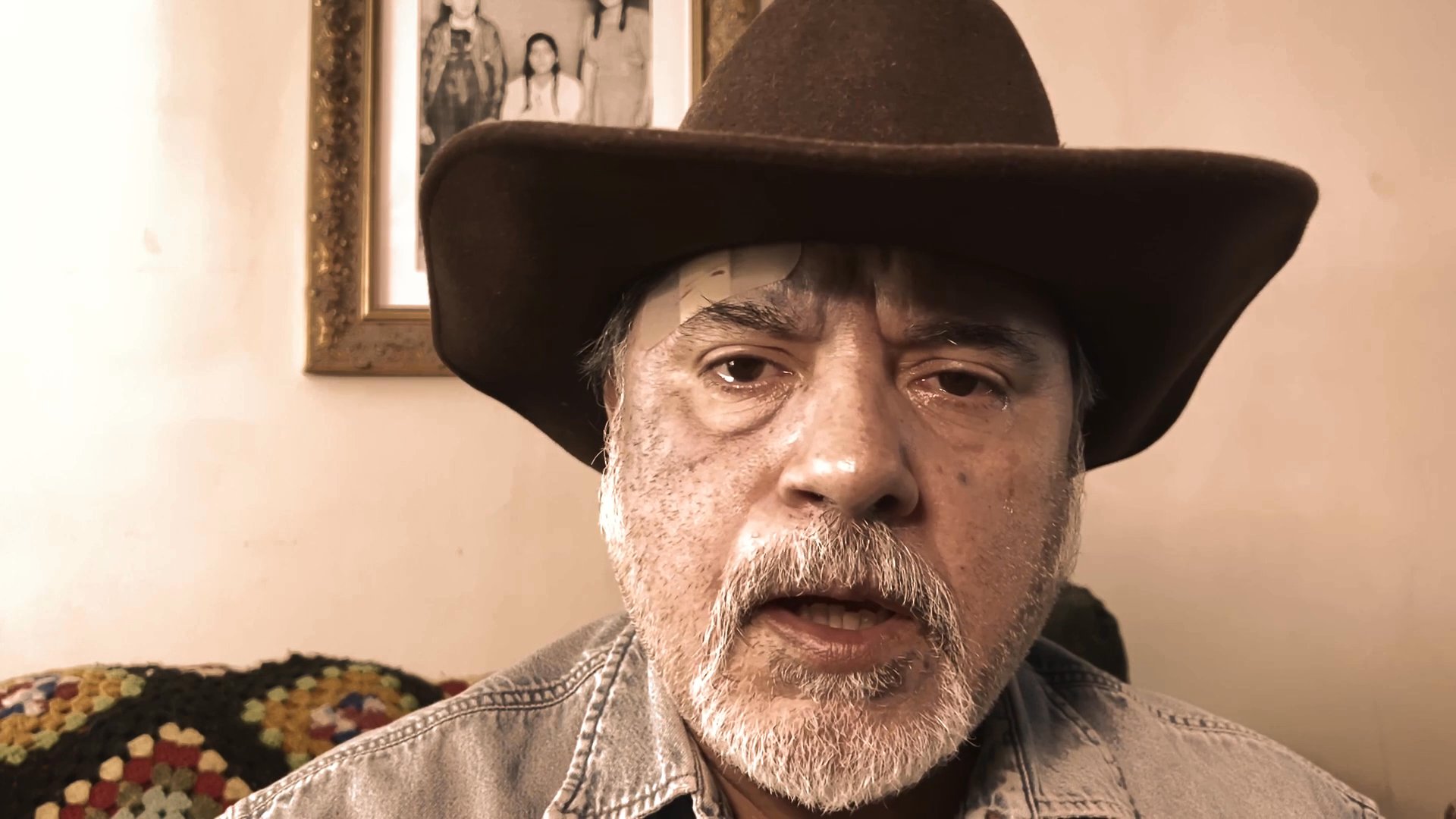 A man wearing a cowboy hat speaks directly to the camera while positioned indoors. He maintains a serious demeanor, delivering a narrative through subtle facial movements and gestures.