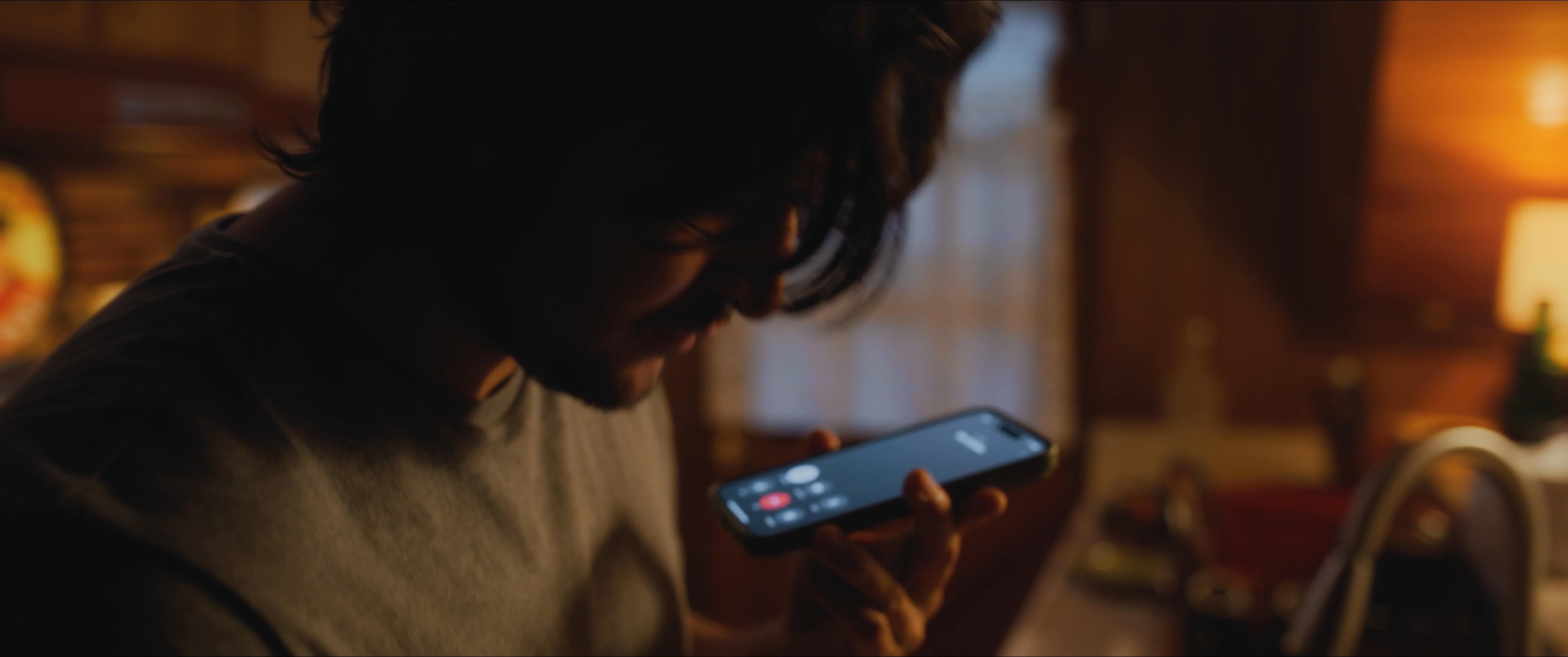 A man engages in a telephone conversation while systematically searching through a cluttered drawer. He retrieves a small, vintage-style commemorative coin and pauses to reflect while maintaining his call.