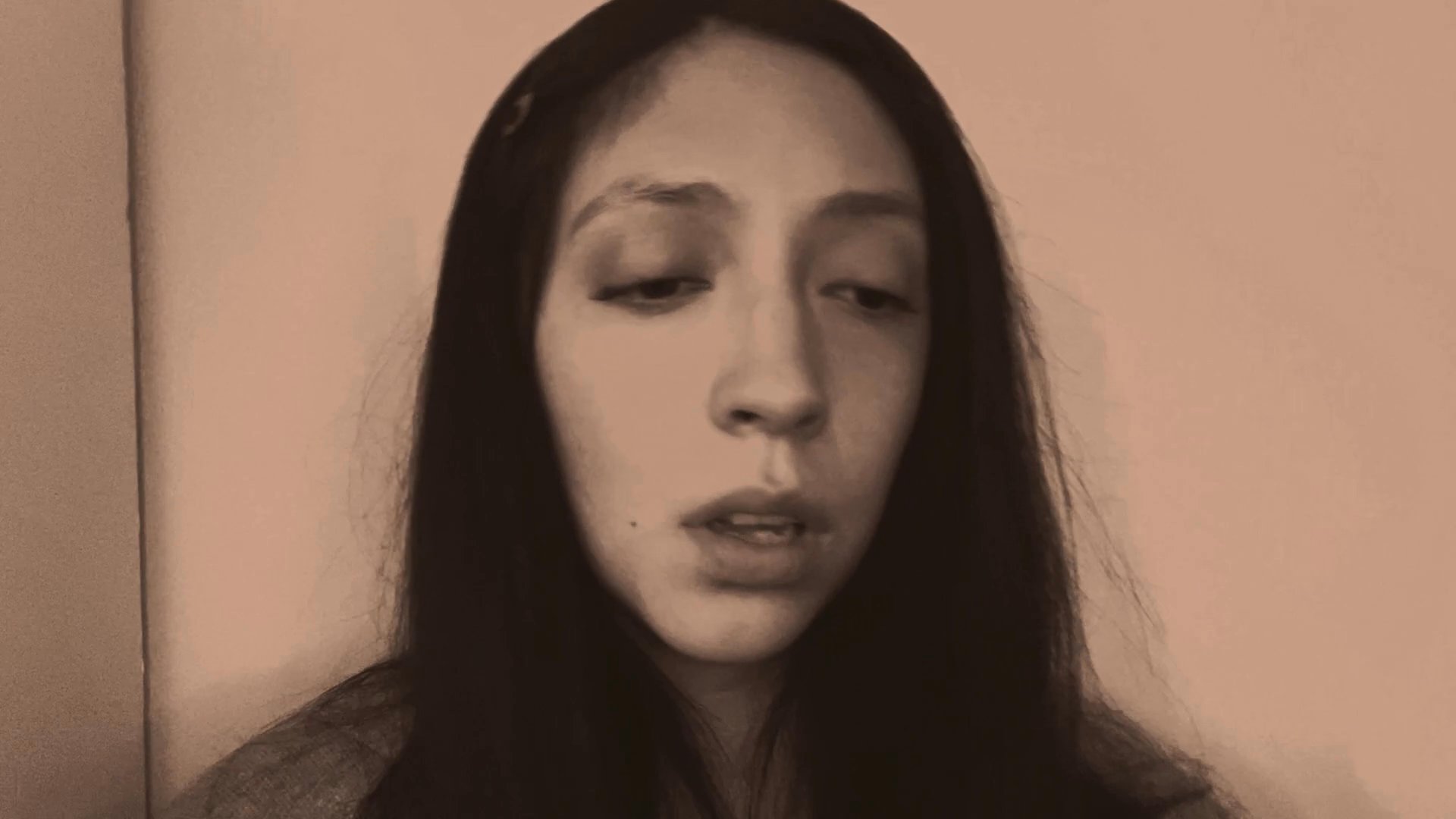 A woman delivers an emotive, expressive monologue while maintaining direct eye contact with the viewer. Her subtle facial changes convey a nuanced narrative arc through performance art.
