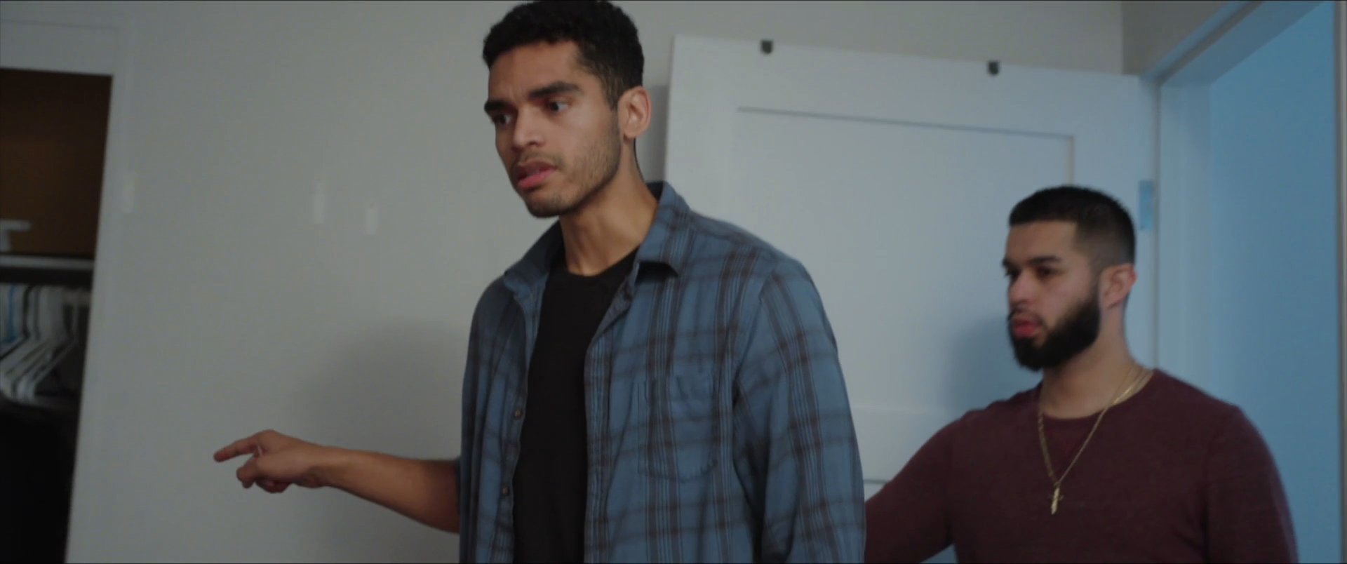 A man finishes a phone call in his bedroom while two friends observe and join the conversation. The group interacts in a casual residential setting.