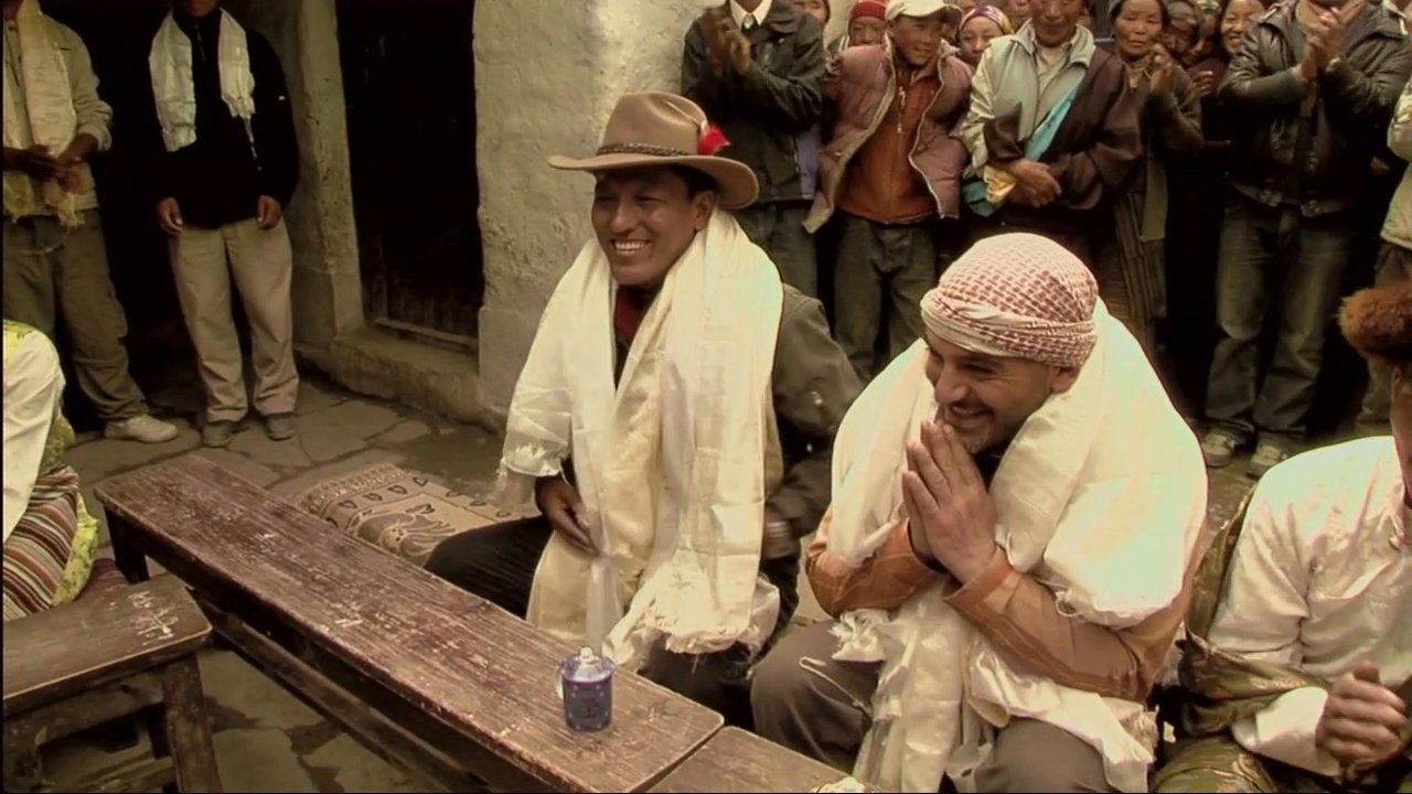 Local children and adults in a Himalayan community perform a traditional khata scarf ceremony to welcome visitors. This gesture of honor and respect is followed by a commentary segment detailing the cultural significance of the event.