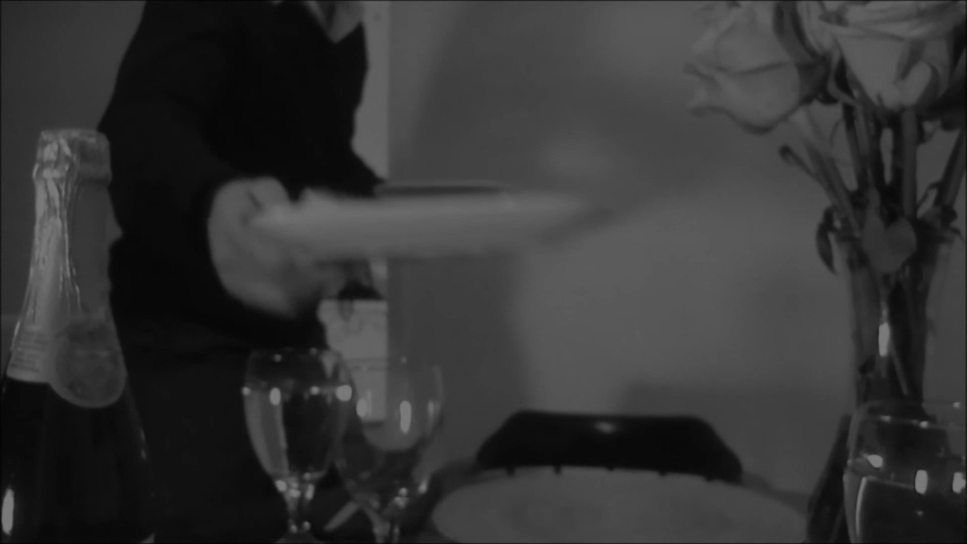 A man speaks on the telephone while setting a formal dining table for an intimate meal. He meticulously arranges plates and glassware to complete the evening setup.