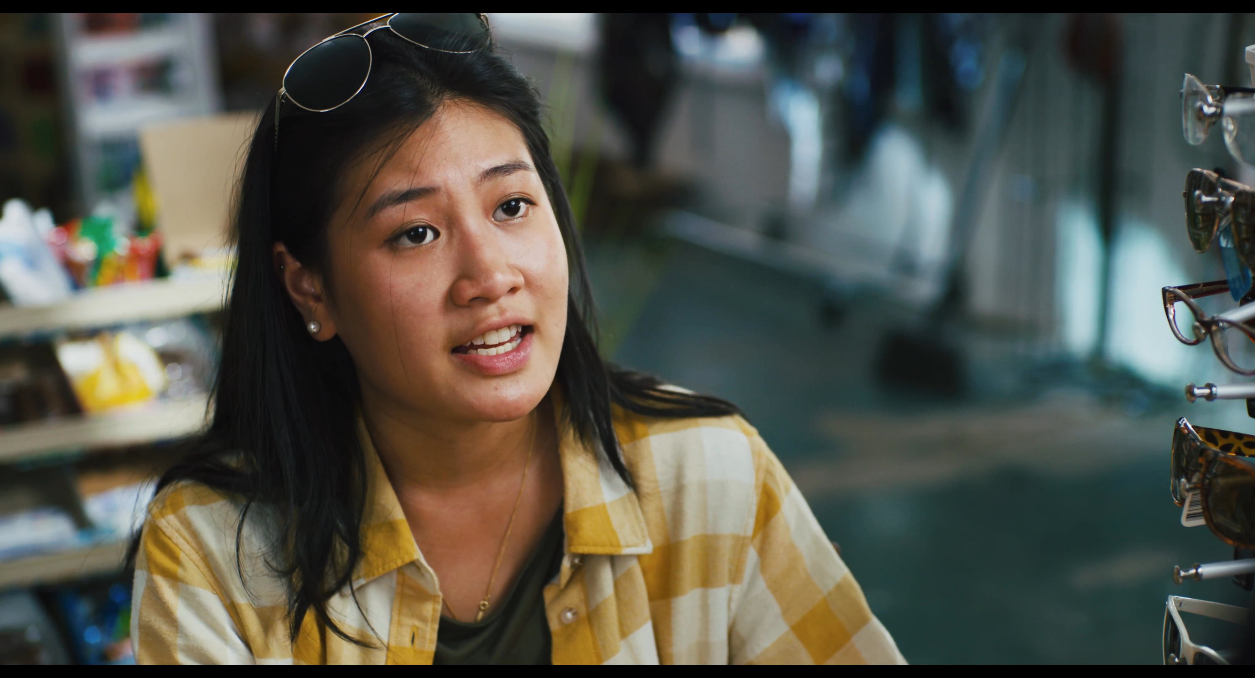 A man wearing a company uniform engages in a serious conversation with a woman inside an eyewear retail store.