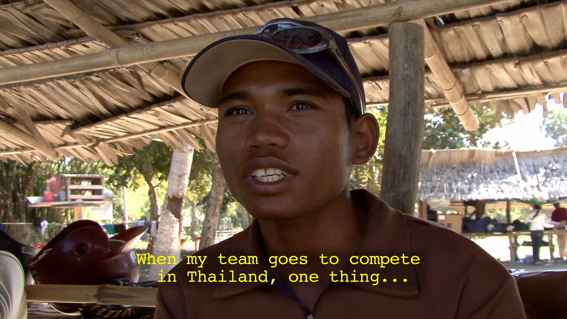 A young athlete discusses his team's goals and first-time experience competing in Thailand, interspersed with shots of team members washing outdoors.