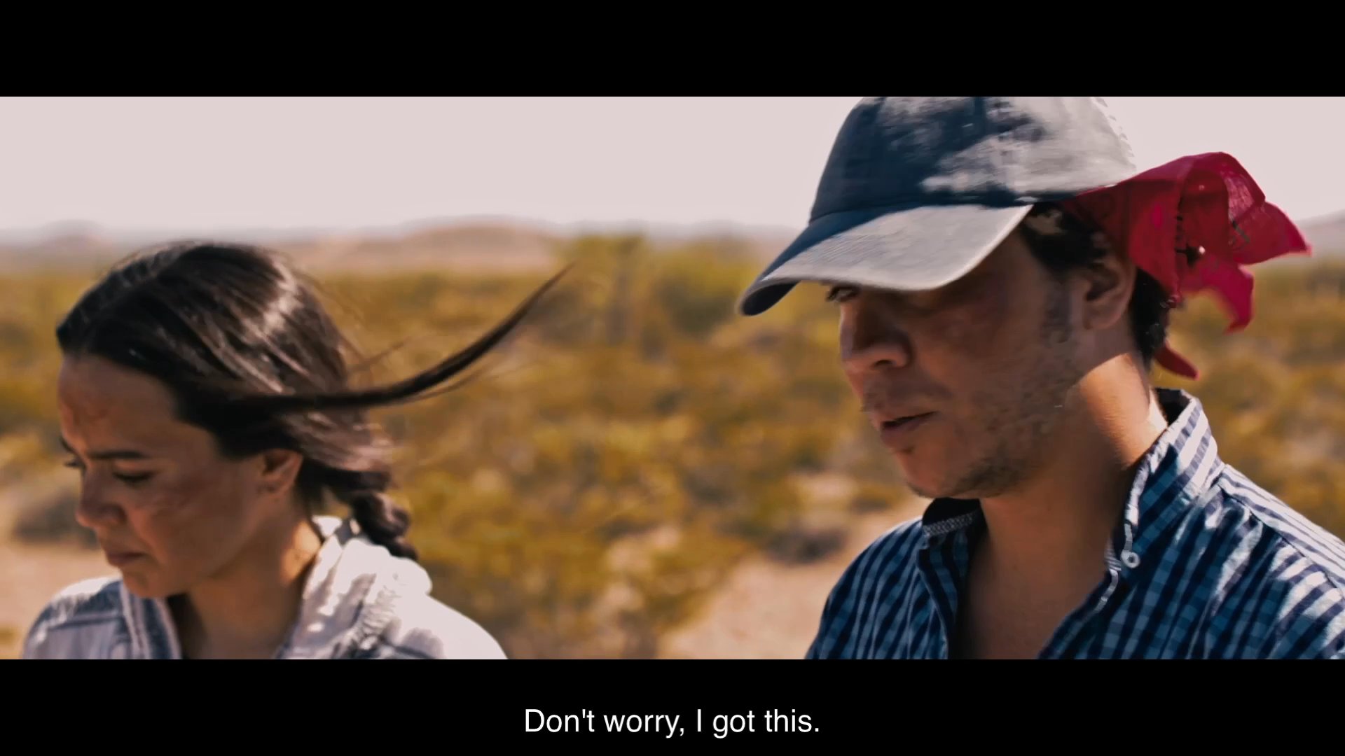 Two individuals navigate a tense encounter in a remote desert setting while preparing to approach a third party. The scene emphasizes escalating interpersonal conflict through rapid dialogue and a stark, desolate environment.