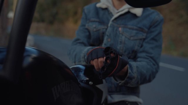 A motorcyclist putting gloves on by the roadside