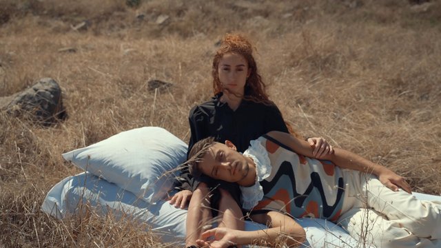 A man and woman are on a bed in the middle of a field