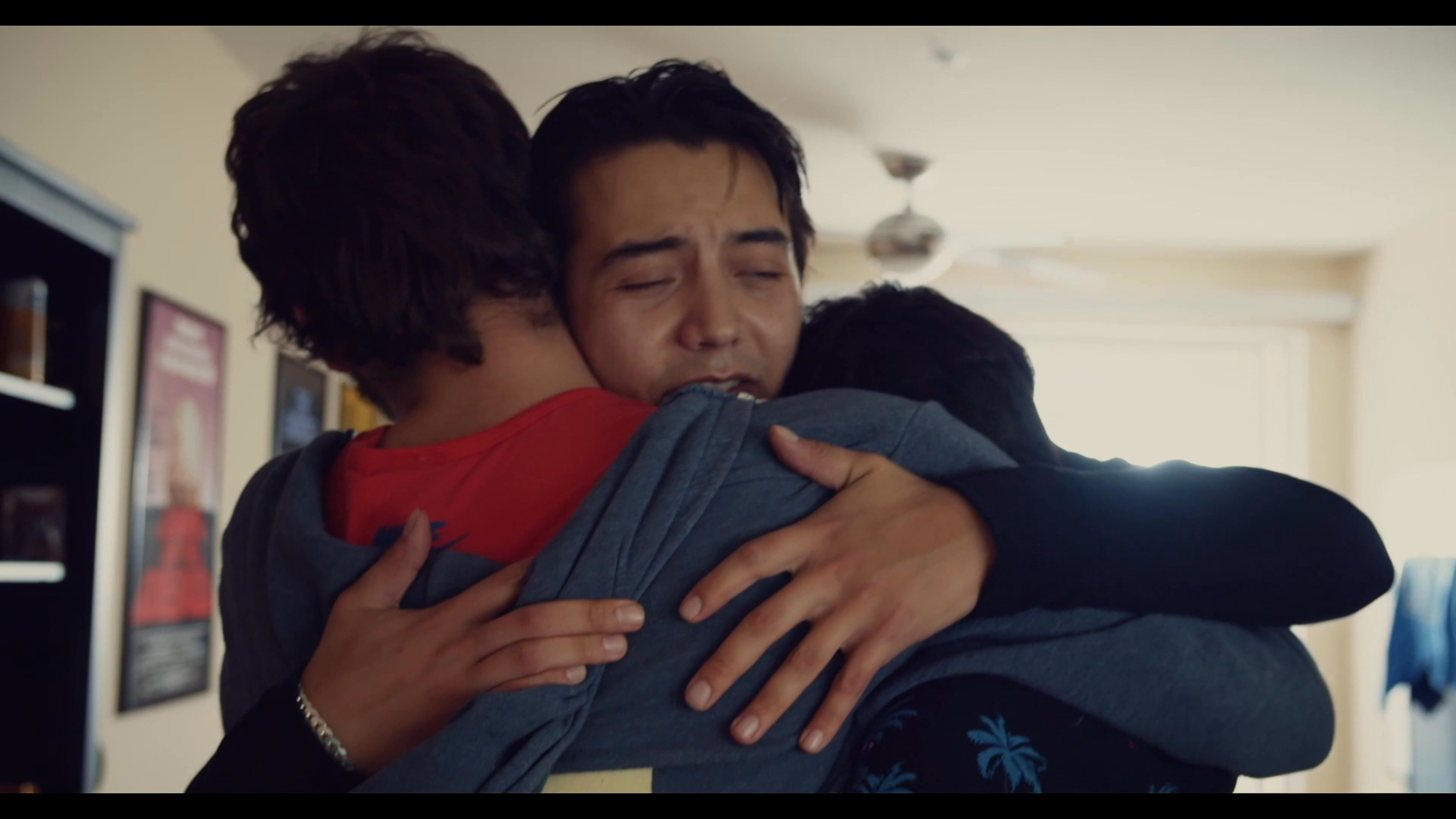 A group of friends reunites in an apartment, sharing an emotional embrace and warm welcome upon arrival.