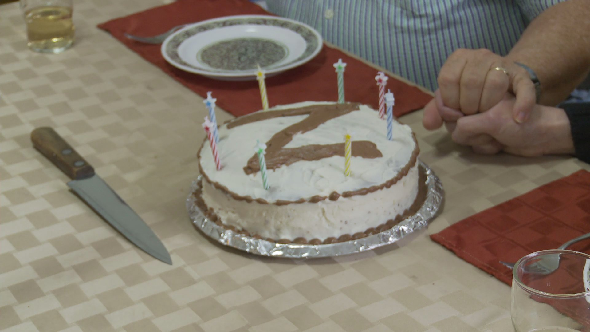 A man and woman share an intimate anniversary celebration at their home, featuring a cake marked with a Z and a heartfelt conversation.