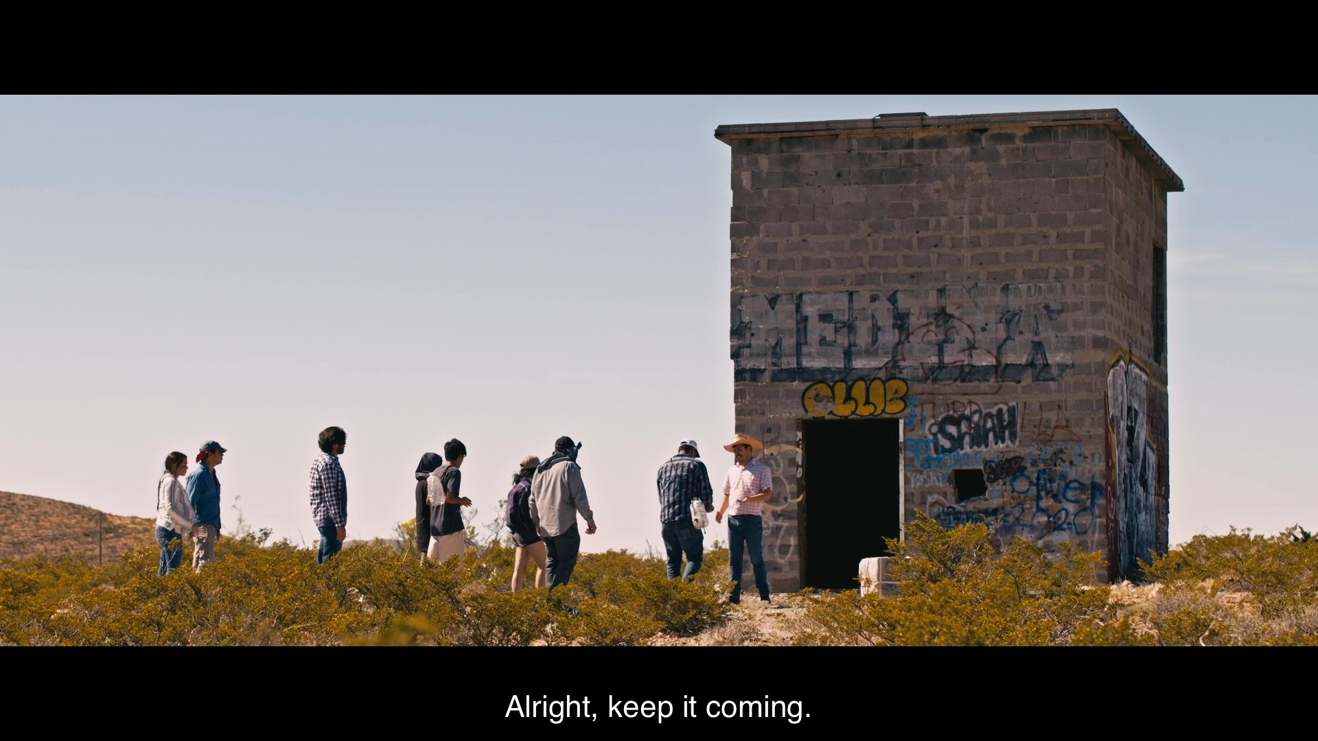 A woman engages in a tense domestic interaction before the scene shifts to an arid landscape where individuals are held under duress by armed figures.