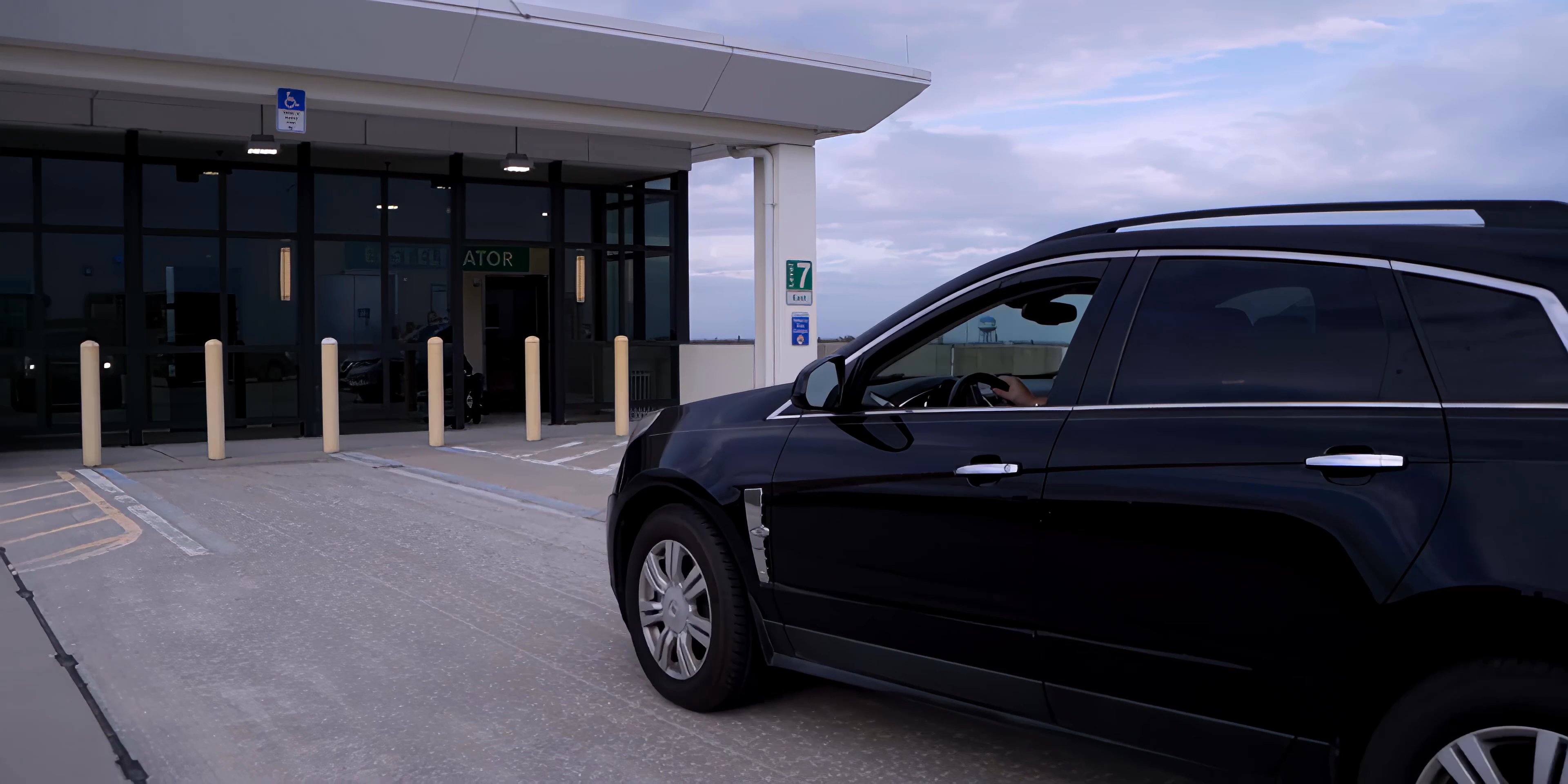 A dark SUV arrives at the rooftop level of the Jackson Street Garage, where the driver exits to meet colleagues near the elevator entrance.