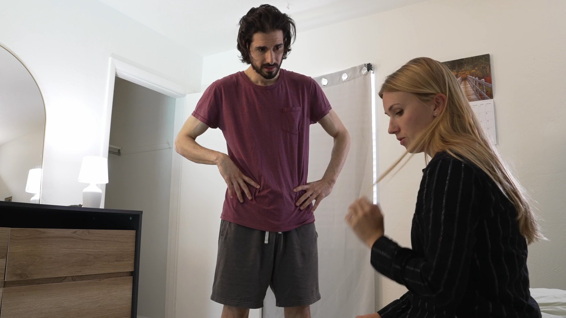 A man and woman engage in a tense, serious conversation within a residential bedroom. The exchange conveys significant emotional weight as the two individuals navigate a difficult interpersonal situation.