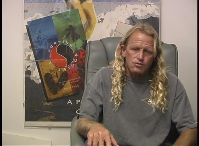 A man with long blonde hair gestures while speaking directly to the camera in an office setting. He maintains a conversational tone throughout the interview.