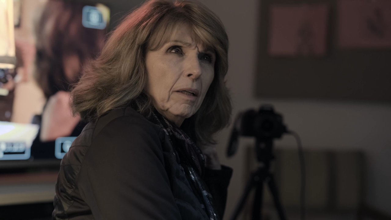 An artist engages in a focused, emotive dialogue with a woman in an art studio equipped with recording technology. The pair navigates a thoughtful interaction amidst canvas paintings and studio lighting.