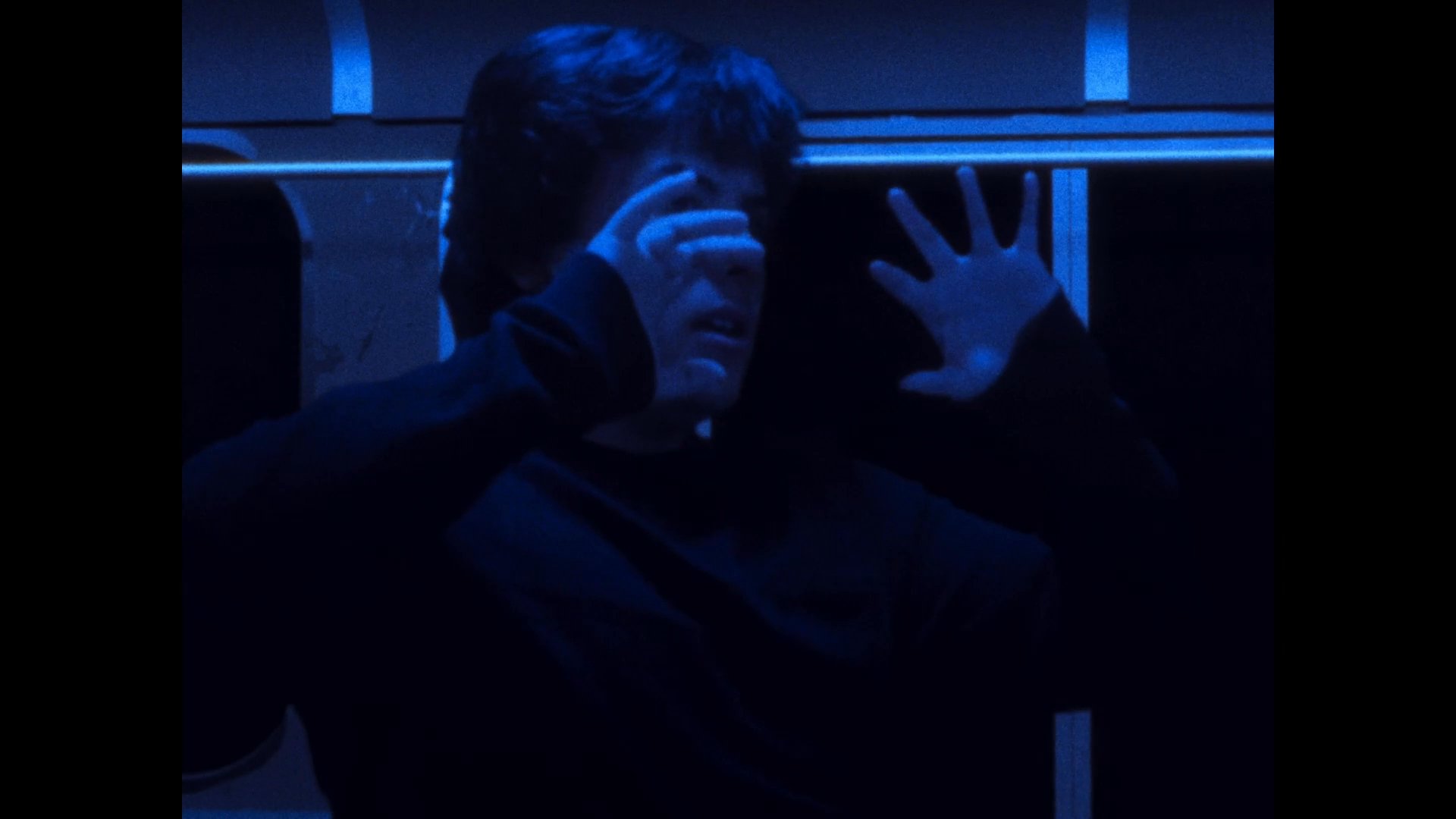 A passenger experiences a heightened state of agitation and distress while traveling alone in a dimly lit, blue-hued train carriage.