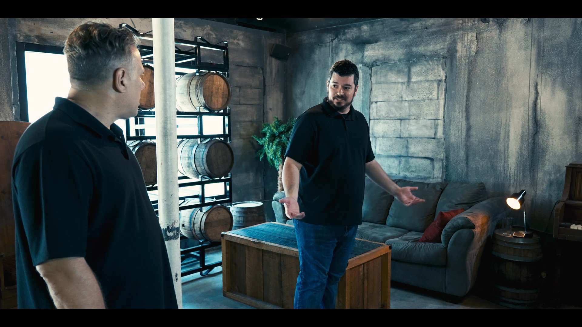 Two men engage in a professional conversation within a contemporary, rustic-styled interior, discussing details while navigating the space. They interact deliberately, highlighting a collaborative exchange in a controlled environment.