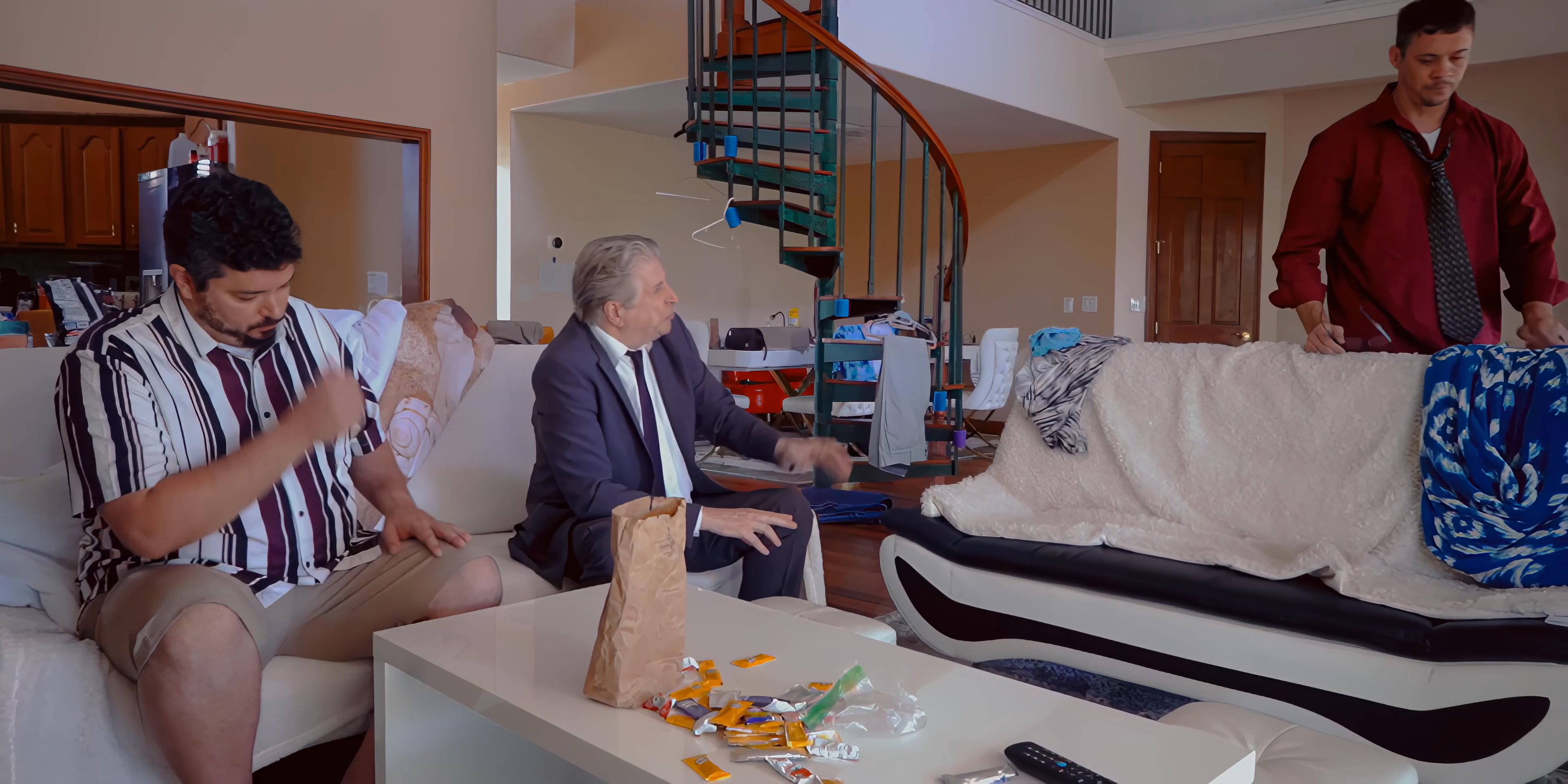 Three men engage in a tense and heated discussion within a living room setting, characterized by visible frustration and interpersonal conflict.