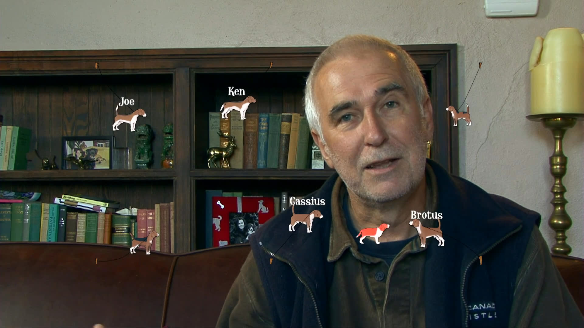 A man speaks directly to the camera during an interview session while a professional videographer records the interaction in a residential setting.
