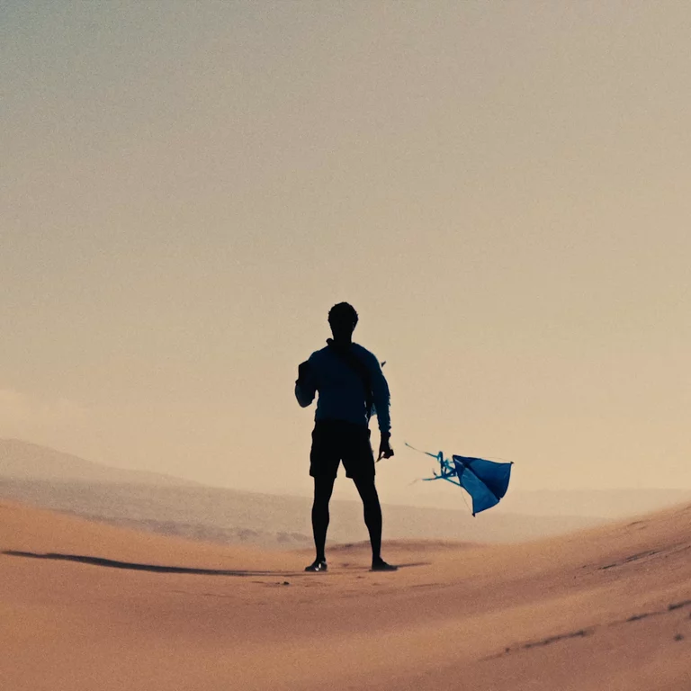 Video of silhouetted man standing in Moroccan sand dunes flying a kite blowing in the wind