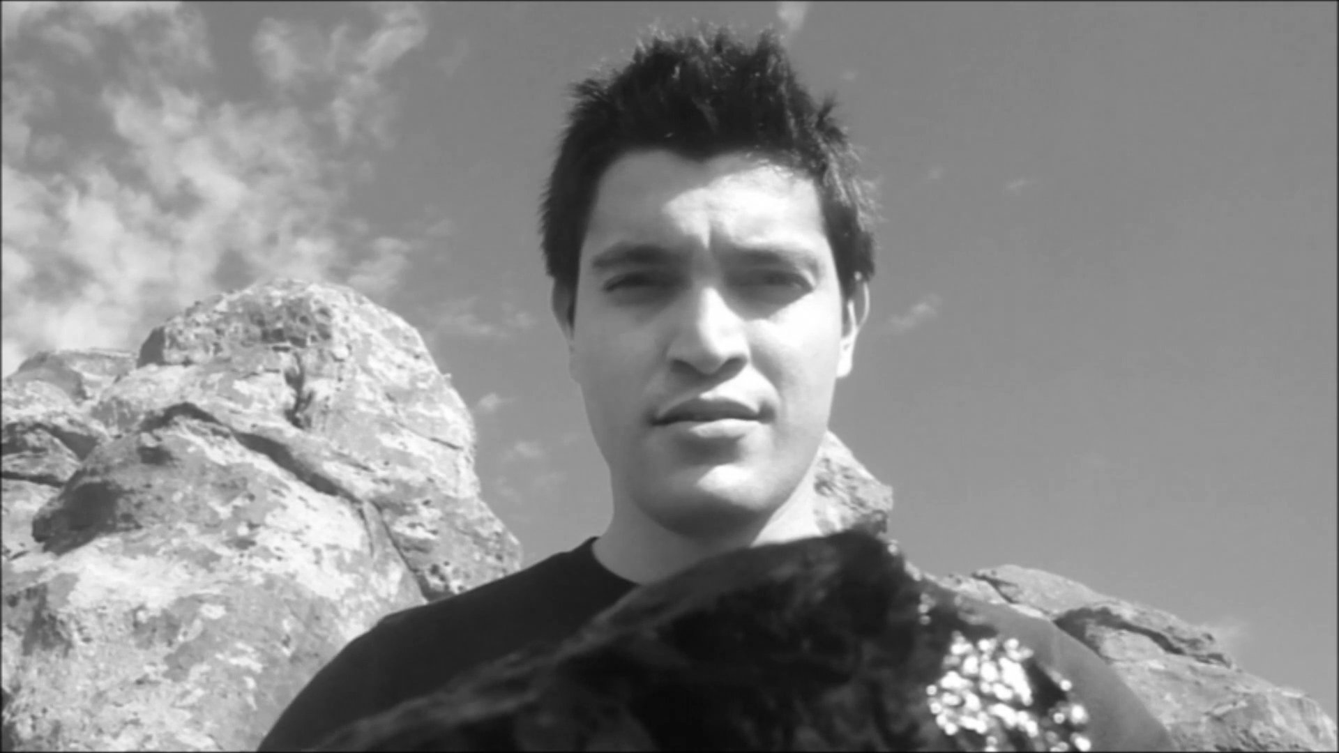 A man captures a selfie in front of a natural rock formation while outdoors. The sequence highlights the person interacting with the environment, emphasizing the scale and texture of the terrain.