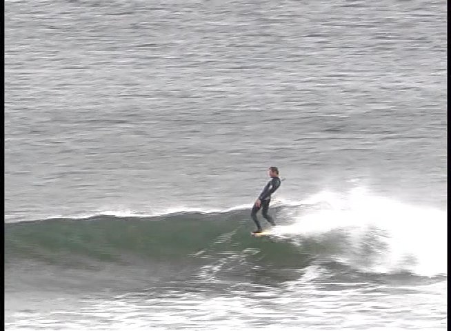A surfer rides waves in the ocean followed by a close-up interview with a man, Harry Mayo, set against a background image of a coastal structure.