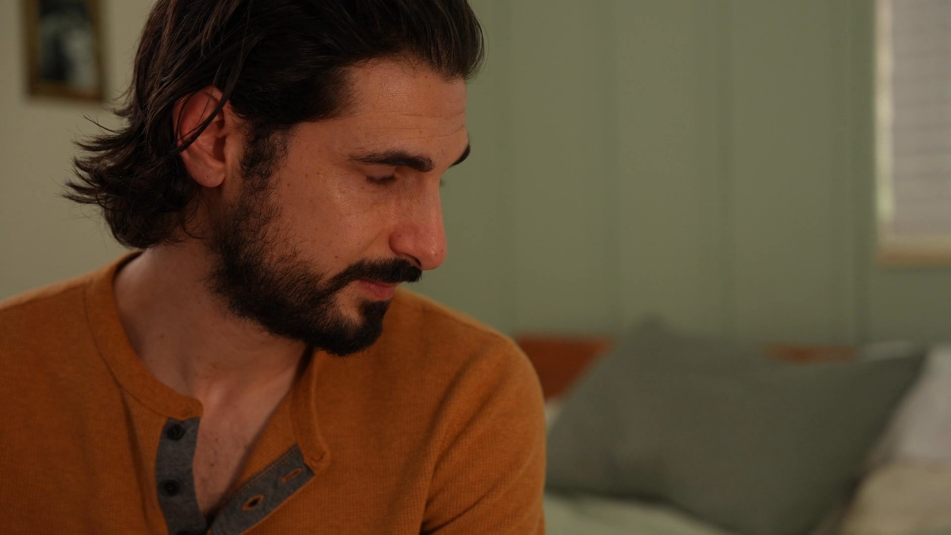 A man watches over a woman as she sleeps in a bedroom. The scene conveys a quiet, personal moment of care and companionship within a home setting.