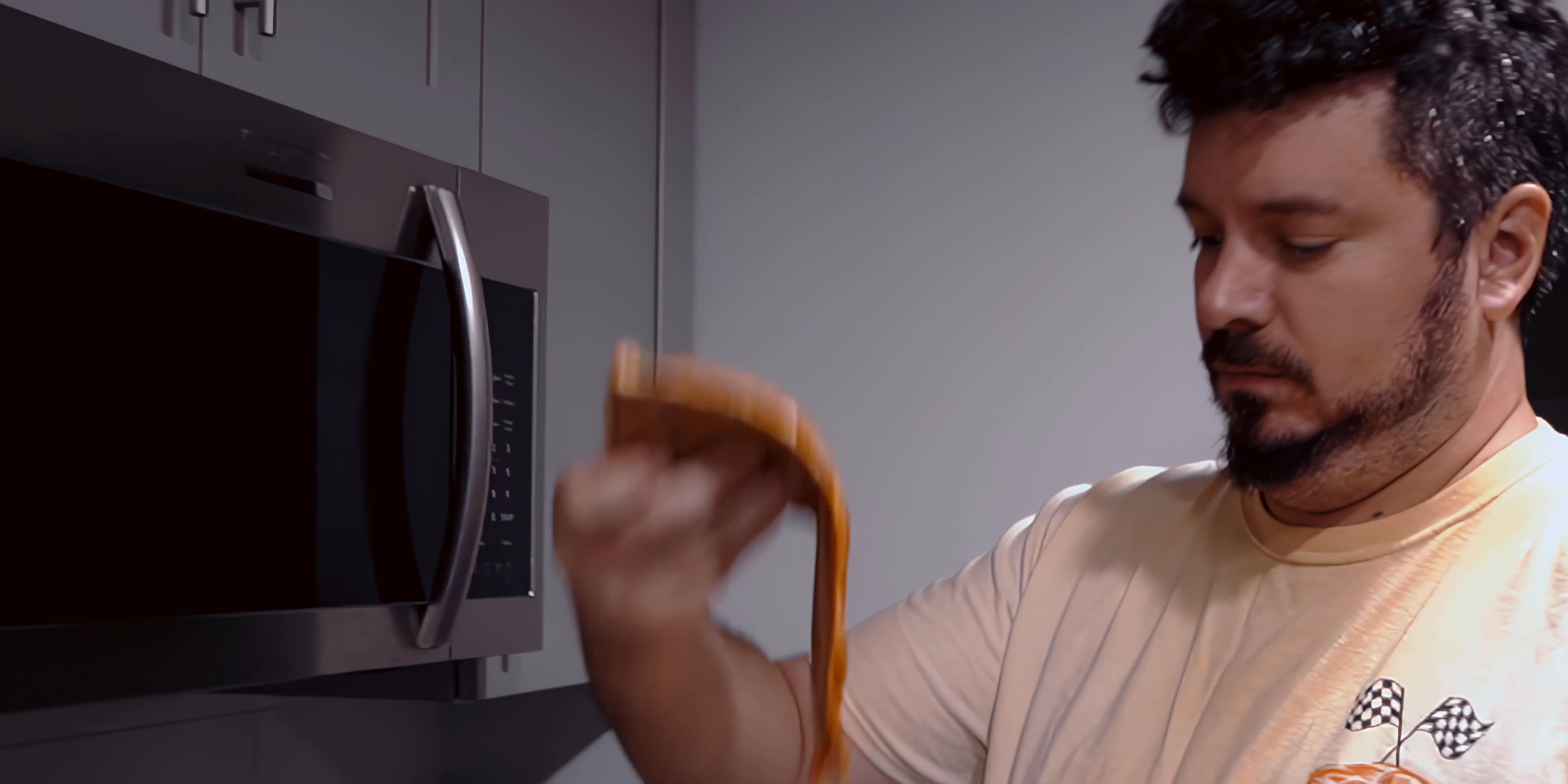 A man prepares a snack in his kitchen, using the microwave to heat food before enjoying it alongside a beverage.