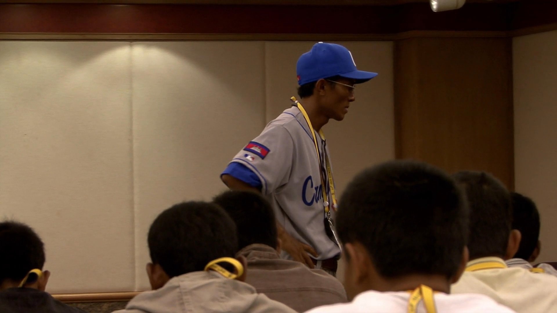 A coach addresses a group of athletes in a seminar setting, delivering a stern lecture on their lack of discipline and national pride. He challenges their commitment to the upcoming competition and their respect for the teaching staff.