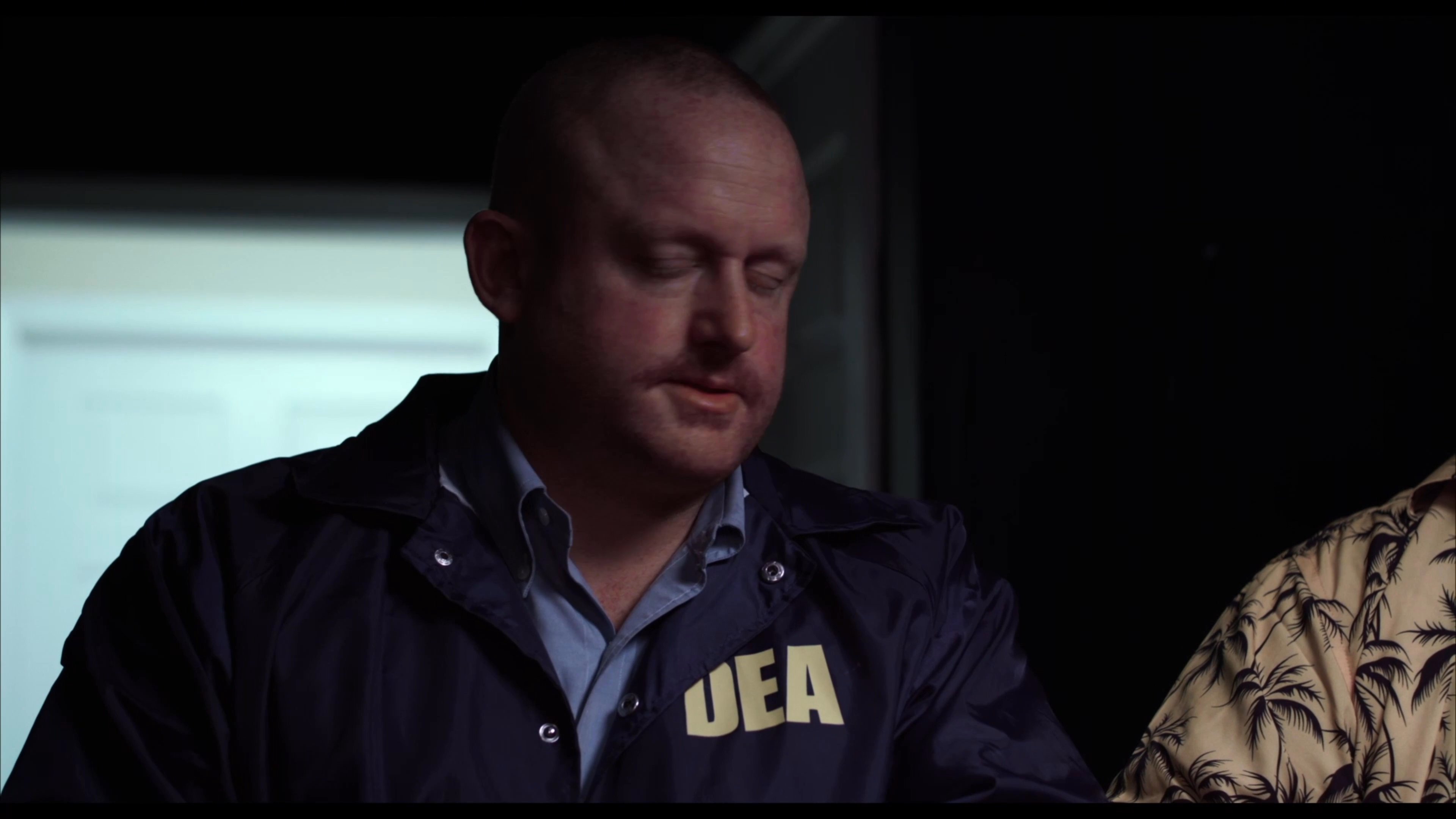 An enforcement officer questions two detainees in orange prison uniforms during a tense, stylized confrontation.