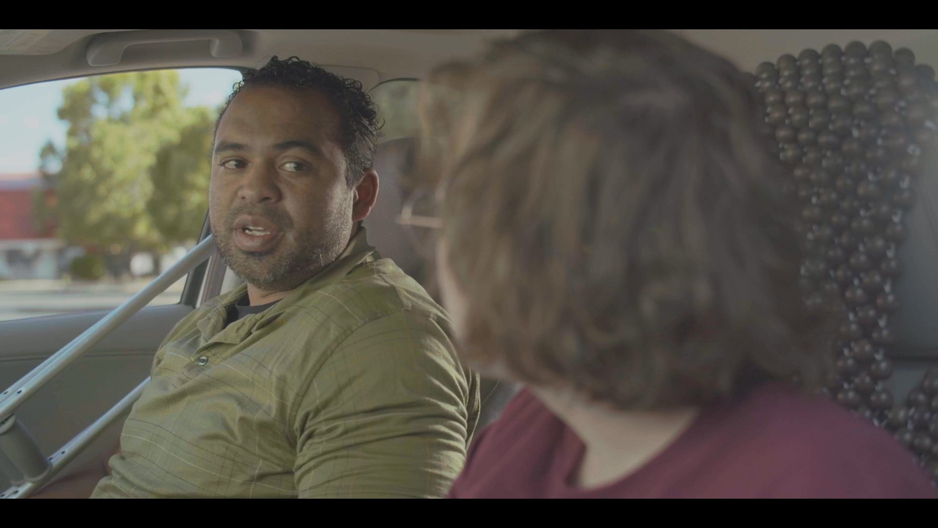 Two individuals engage in a detailed conversation while seated inside a parked vehicle. After concluding their discussion, one passenger exits the car in an outdoor parking lot.
