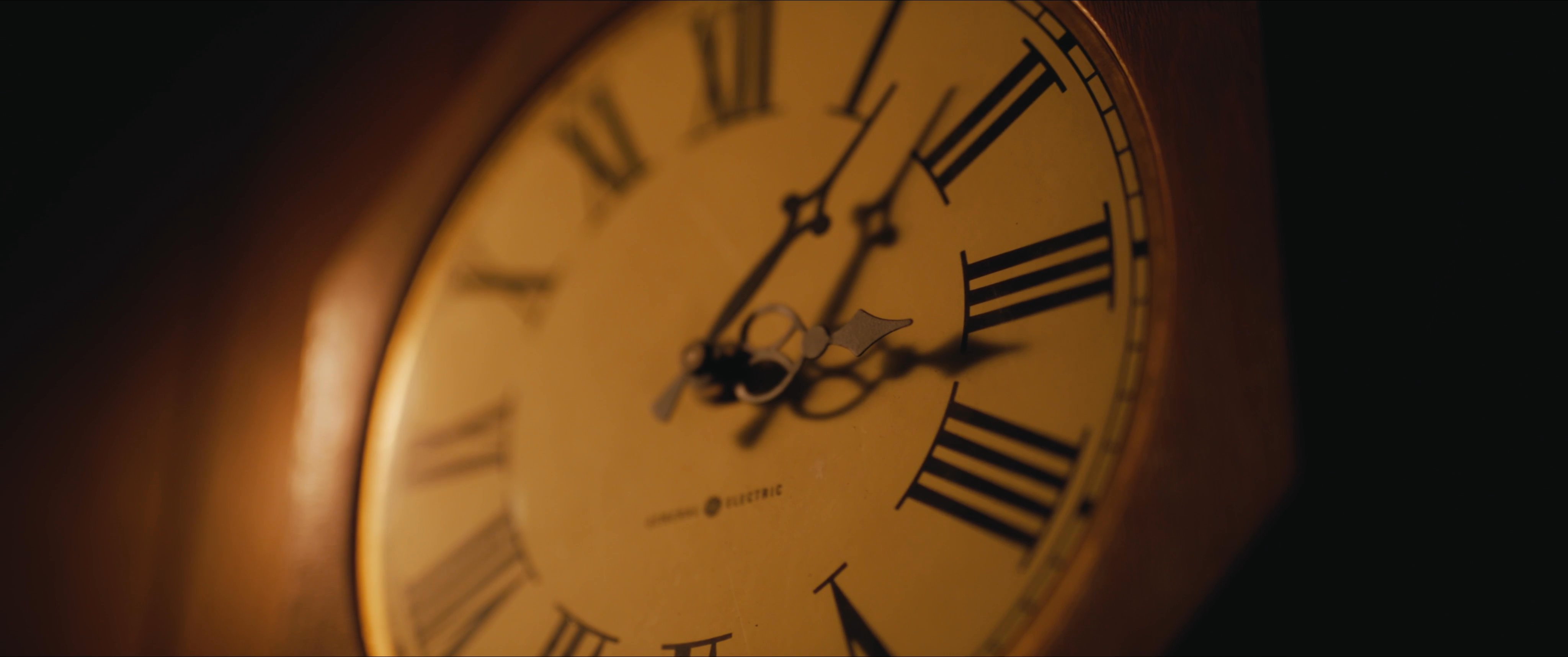 A man sits alone in a dimly lit room, drinking from a bottle, while time passes slowly as observed through a wall clock and ambient décor.