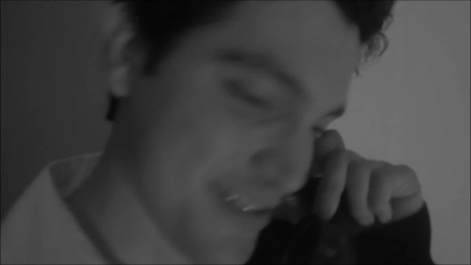 A man engages in a lighthearted phone conversation while standing in a dimly lit, elegantly decorated room. The atmosphere suggests a personal and reflective moment captured in monochrome.