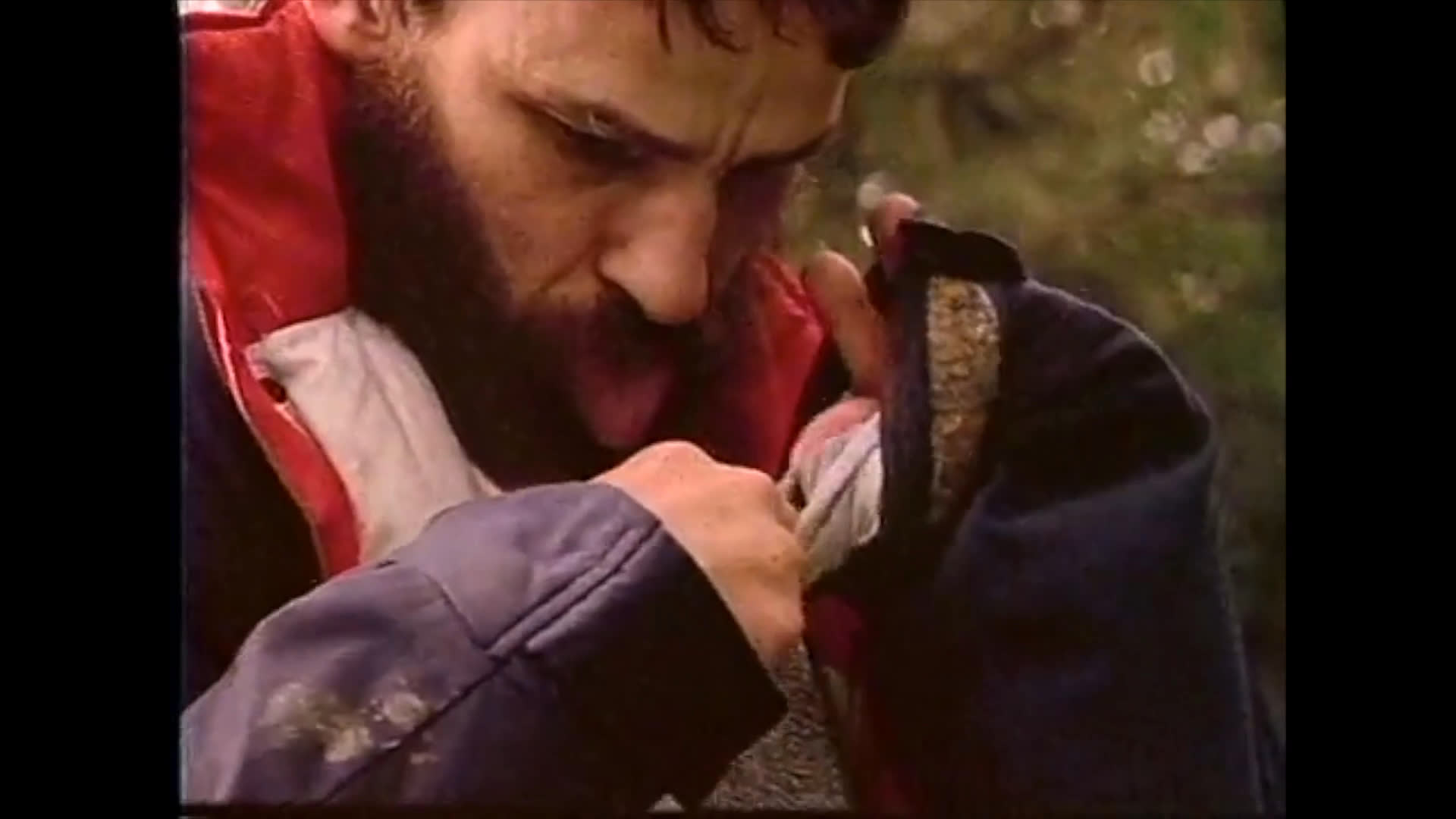 A bearded man in a jacket performs a distinct, expressive hand gesture while outdoors. His intense focus highlights the communicative nature of the movement.