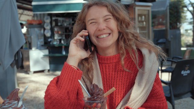 Una niña alegre habla en un teléfono inteligente en un café de la calle