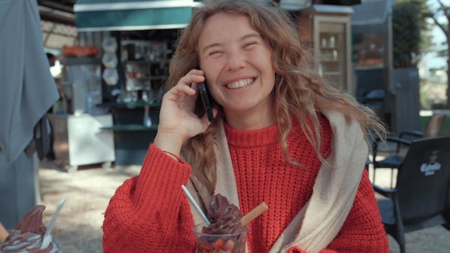 A joyful girl talking on her smartphone at a street café