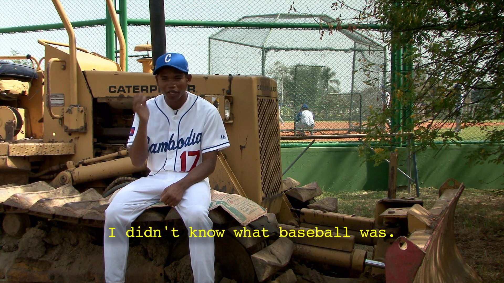 A young baseball player from Cambodia recounts his experience learning the sport using improvised equipment like plastic bags and bamboo sticks. He describes practicing in his youth with friends, detailing how they constructed makeshift gear to develop their skills.